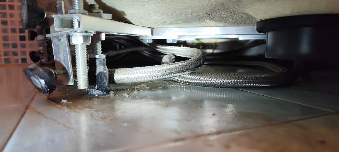 Przeciekający elastyczny wężyk Metalowe elastyczne wężyki pod umywalką z widocznym miejscem przecieku