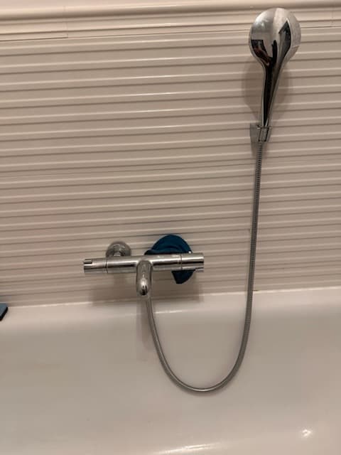 Bateria wannowa srebrna Srebrna bateria wannowa z prysznicem na tle białych płytek