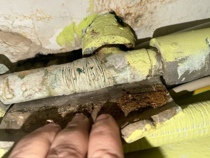 Uszkodzona rura Uszkodzona powierzchnia rury owiniętej taśmą izolacyjną wraz z widoczną ręką pokazującą miejsce uszkodzenia