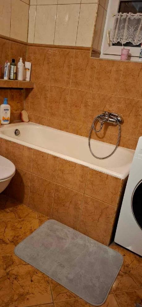 Łazienka przed wymianą wanny Widok łazienki z wanną obitą płytkami ceramicznymi i półką na kosmetyki