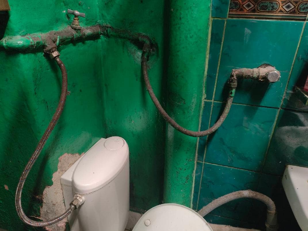Instalacja wodna łazienki Widok na zieloną ścianę łazienki z odsłoniętą instalacją wodną i dwoma elastycznymi przewodami.